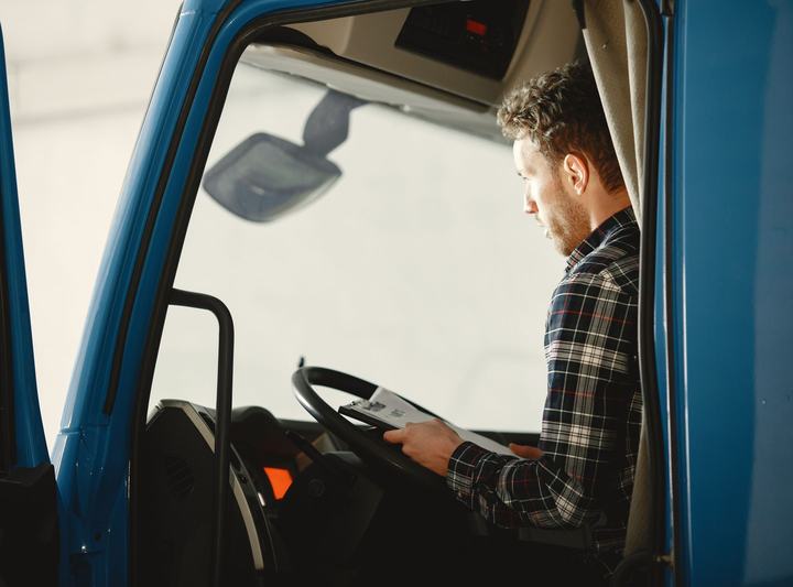 Truck driver in the cab of a blue semi truck reviewing load paperwork