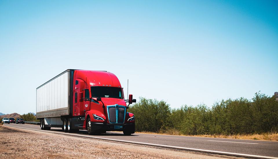 Red semi truck pulling a dry van trailer on a desert highway in the United States